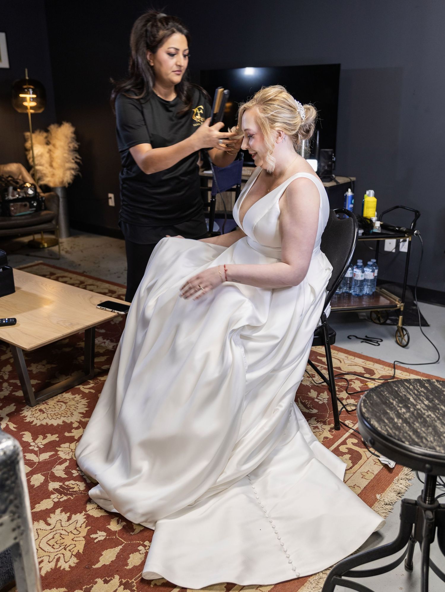 Makeup artist applying makeup to a bride in a white wedding gown before ceremony.