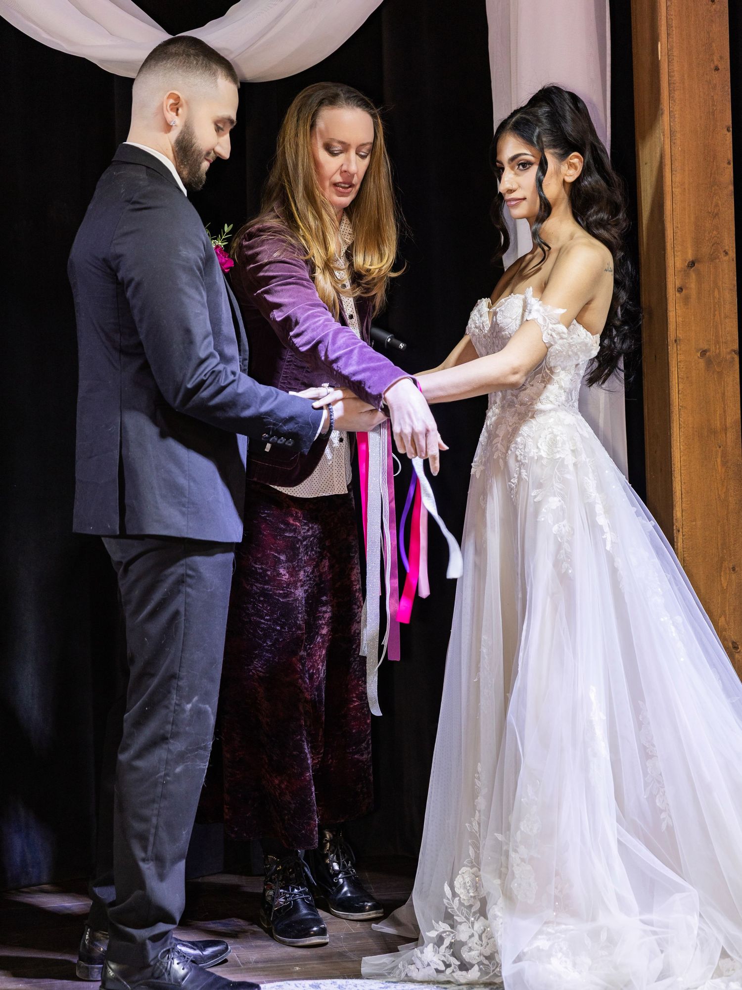 Officiant performing a handfasting ceremony with colorful ribbons for a bride and groom at a wedding.
