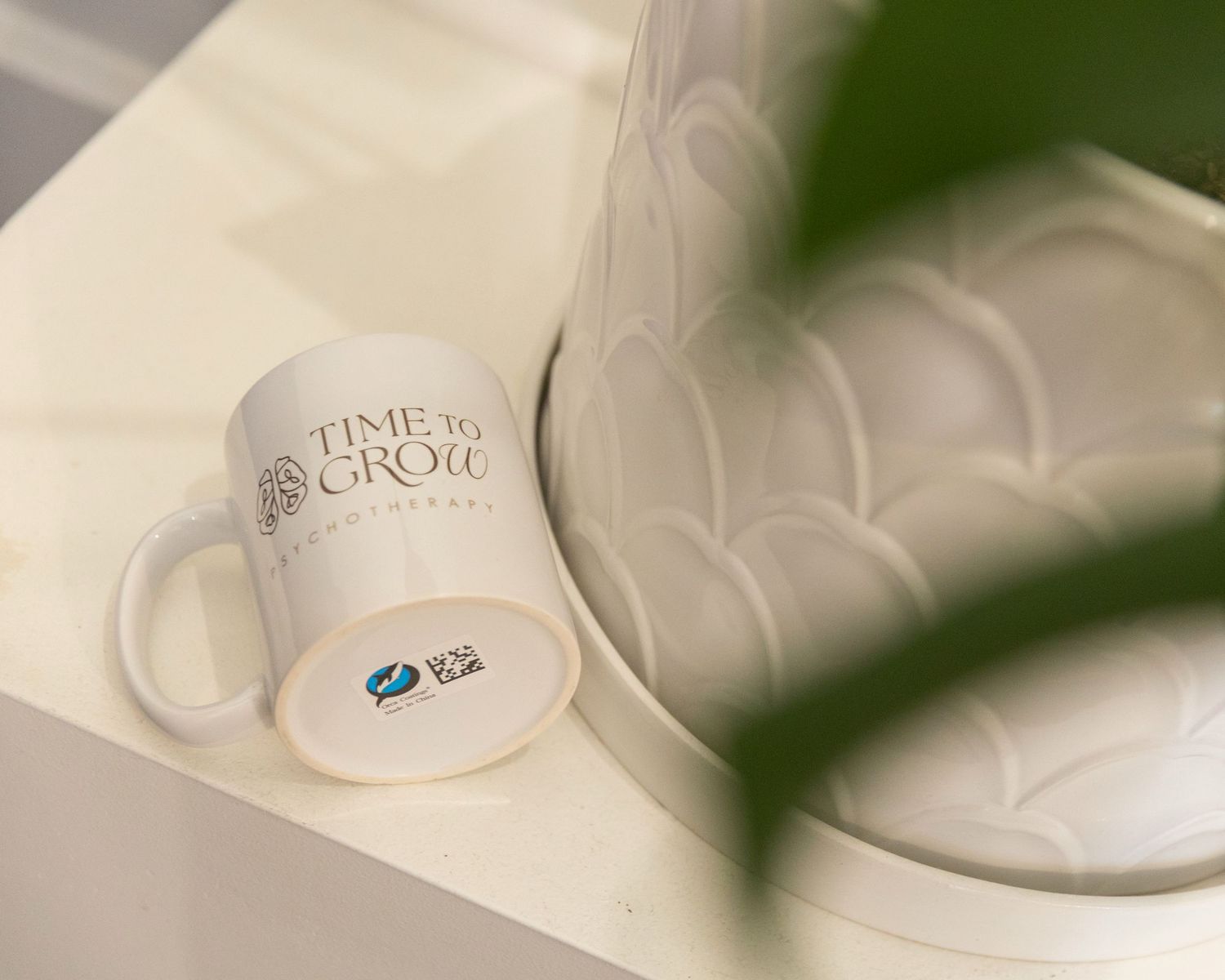 White ceramic mug with Time to Grow slogan on a marble surface beside a decorative vase and green plant.