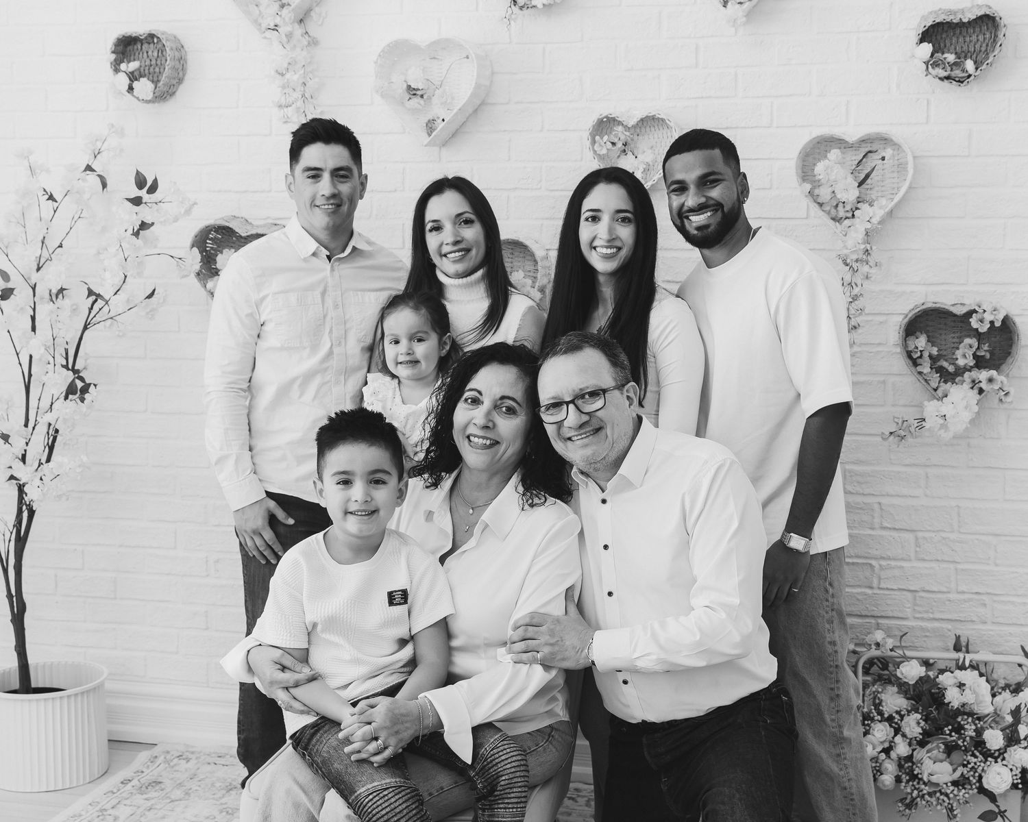 Black and white family portrait of multigenerational group posing with heart balloon decorations.