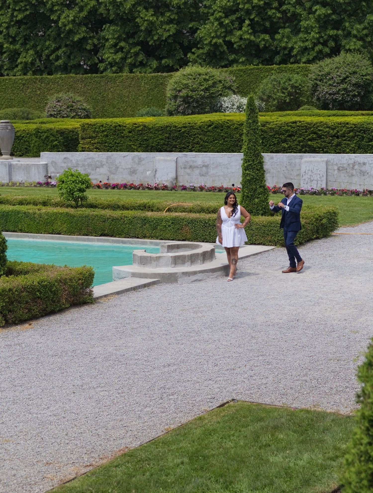 Couple posing in elegant formal garden with manicured hedges and reflecting pool.