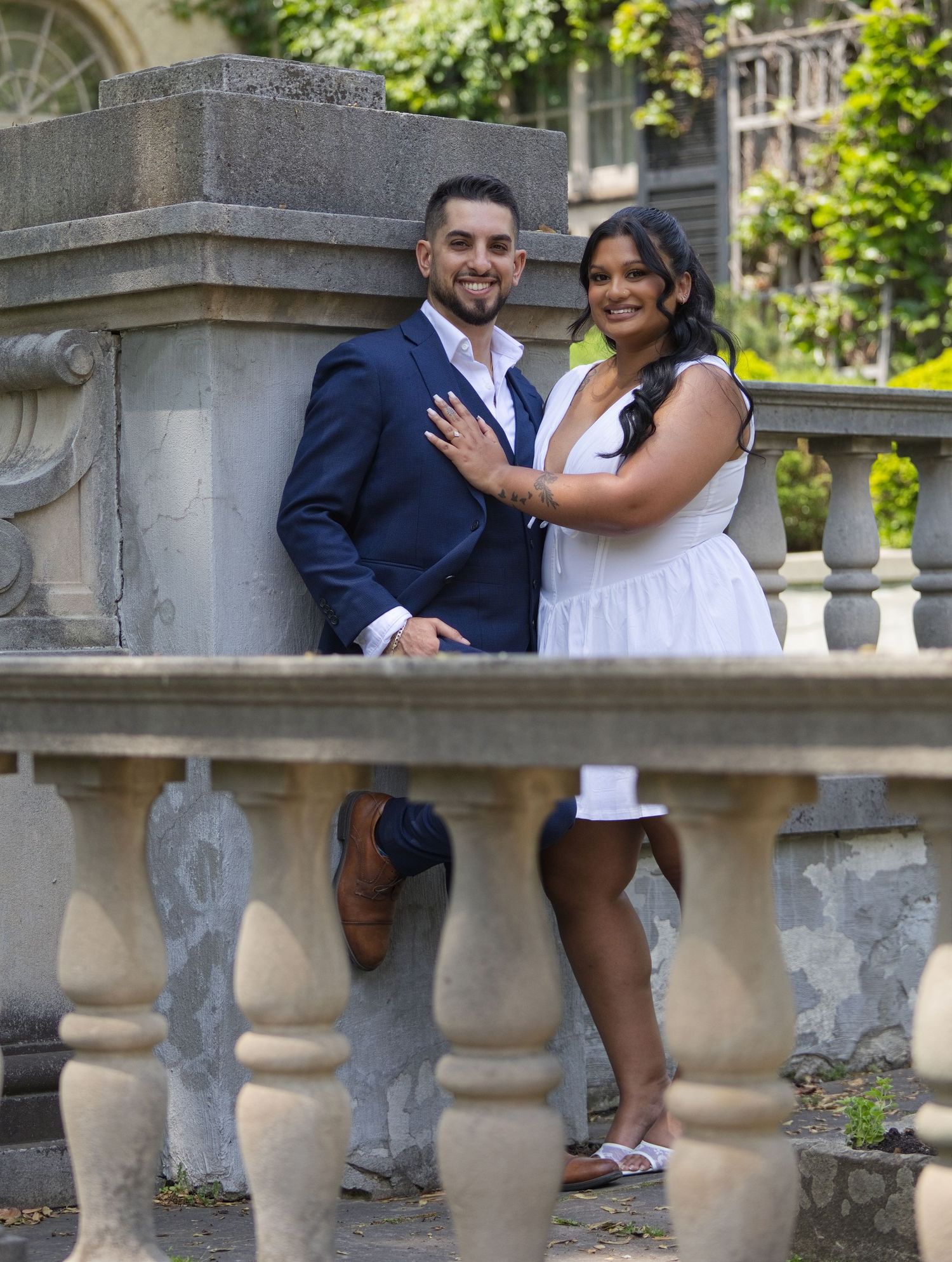 Happy engaged couple posing together at stone balustrade of historic mansion.