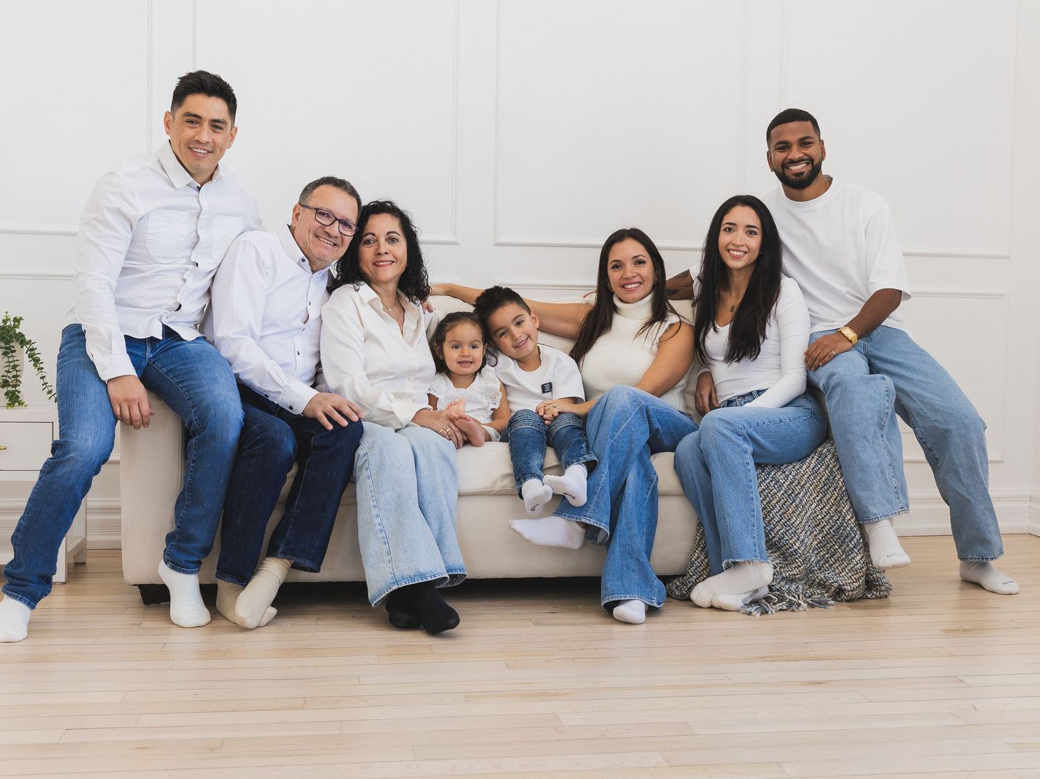 Extended family of eight sitting and posing together on a couch in a white studio.