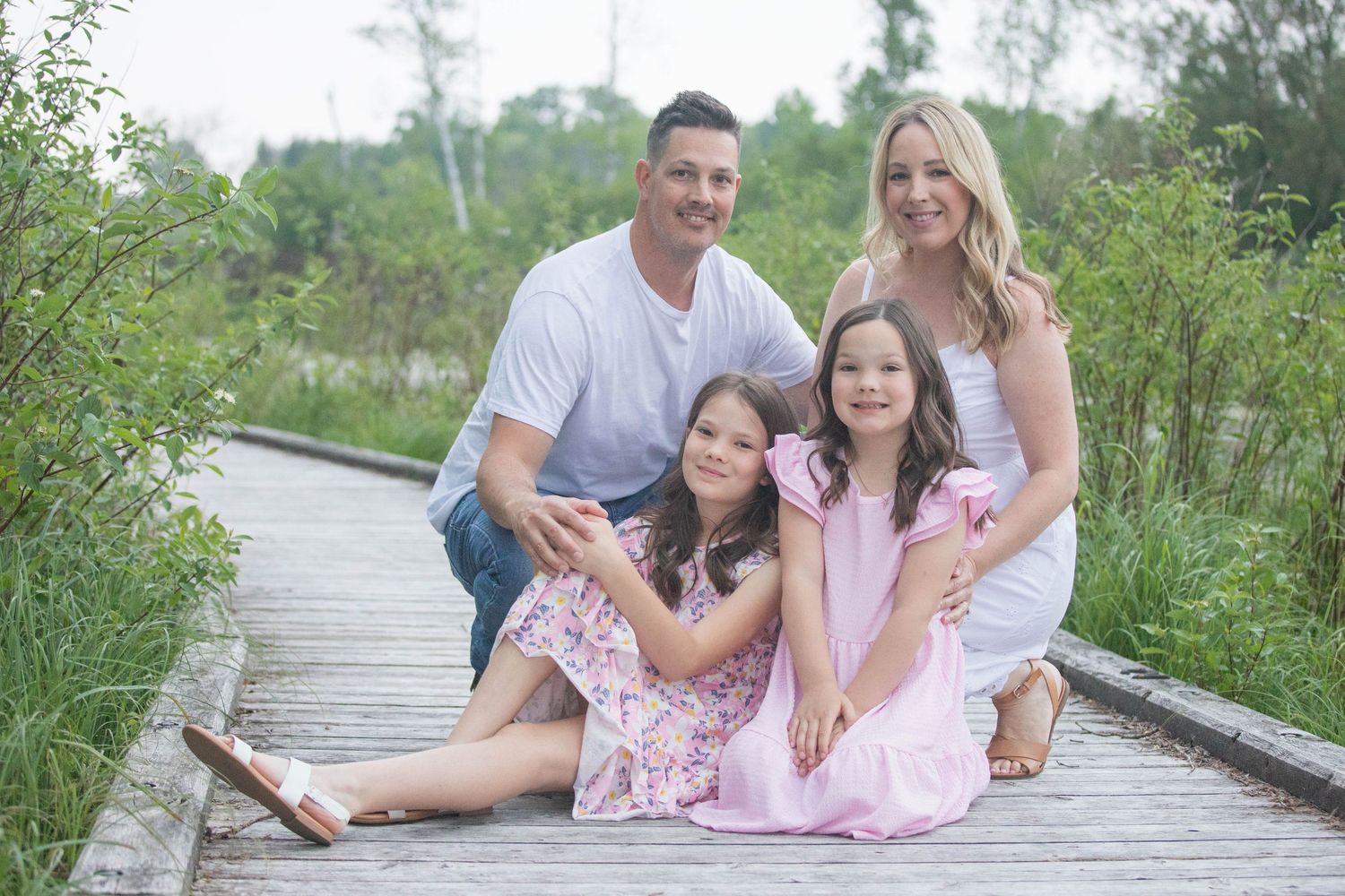 Family of four sitting on wooden boardwalk surrounded by greenery.