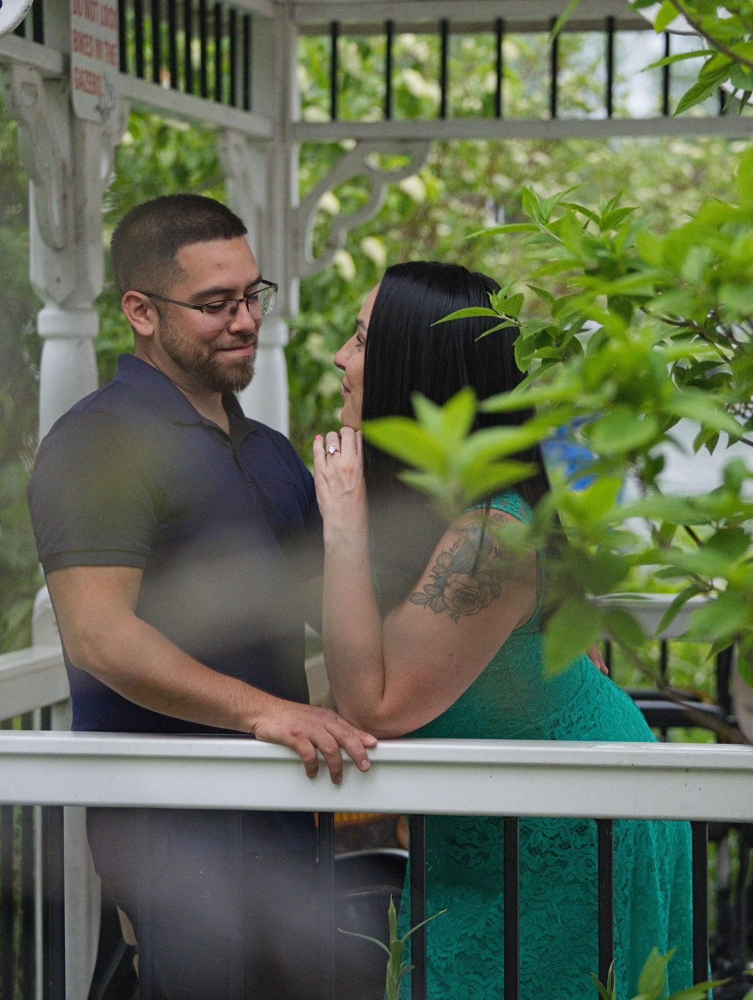 Couple sharing a romantic moment on a white gazebo balcony surrounded by lush green foliage.