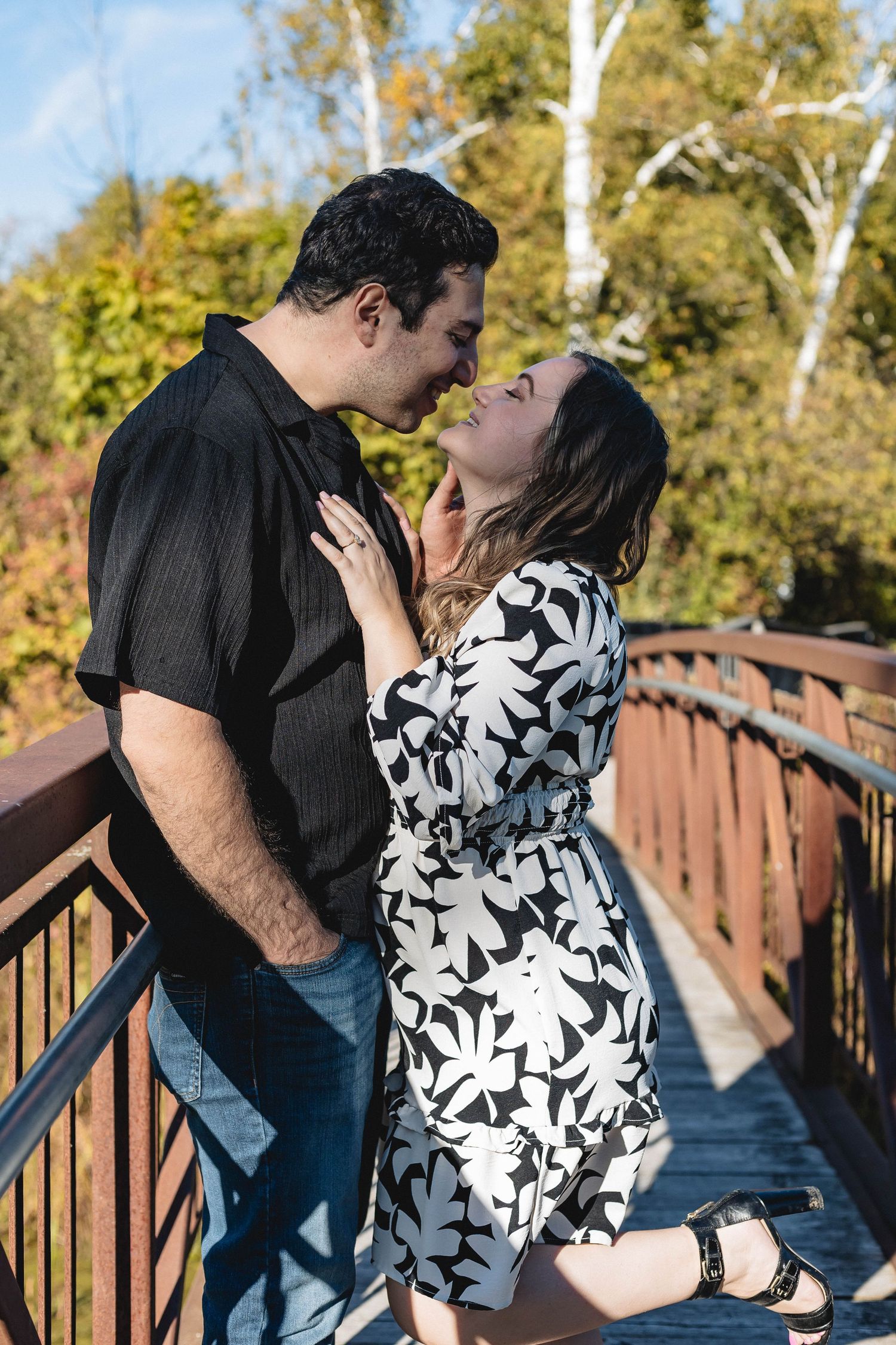 Couple sharing a romantic moment on a wooden bridge surrounded by colorful autumn foliage.