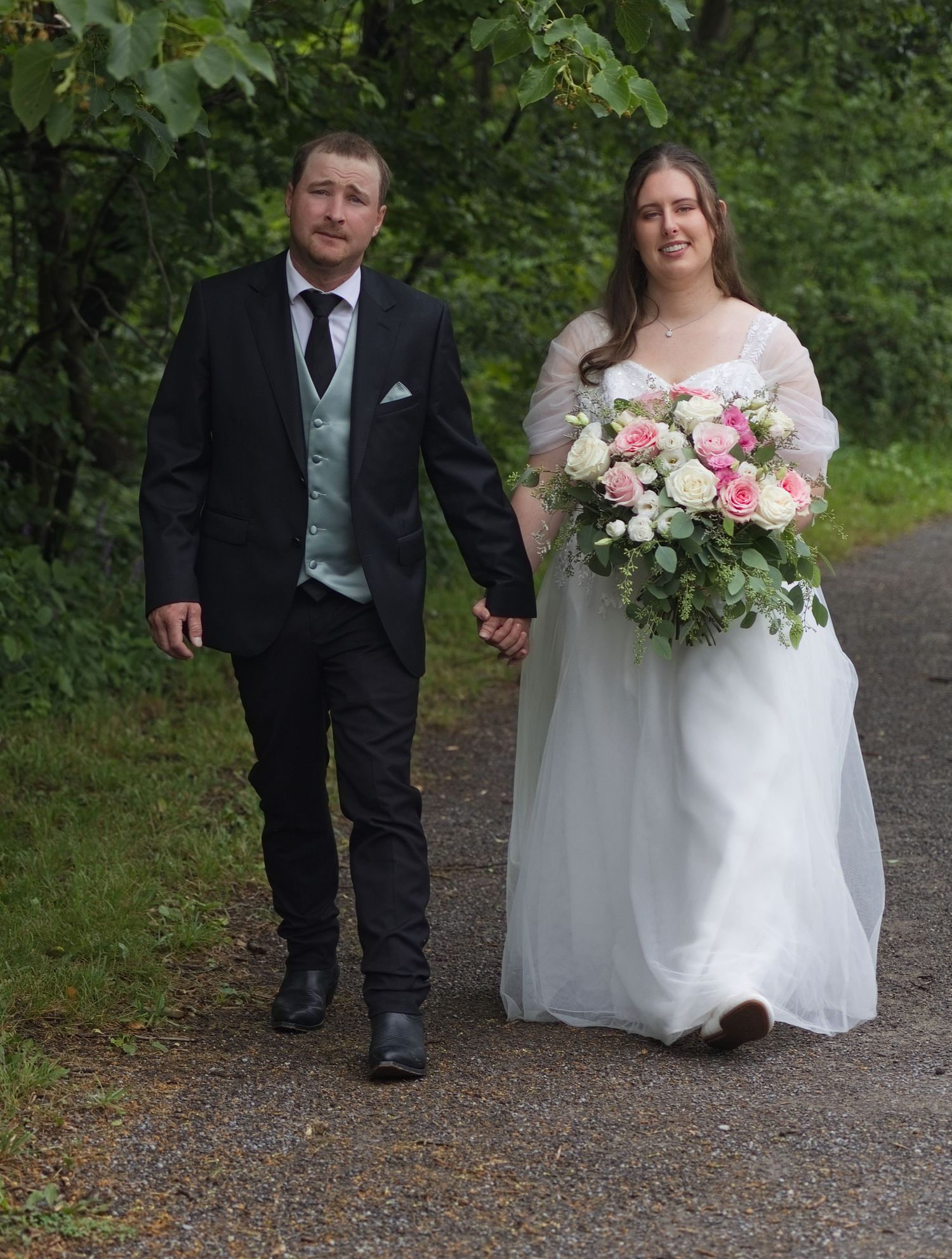 Bride and groom walking hand in hand on a garden path, bride holding pink and white bouquet in white gown.