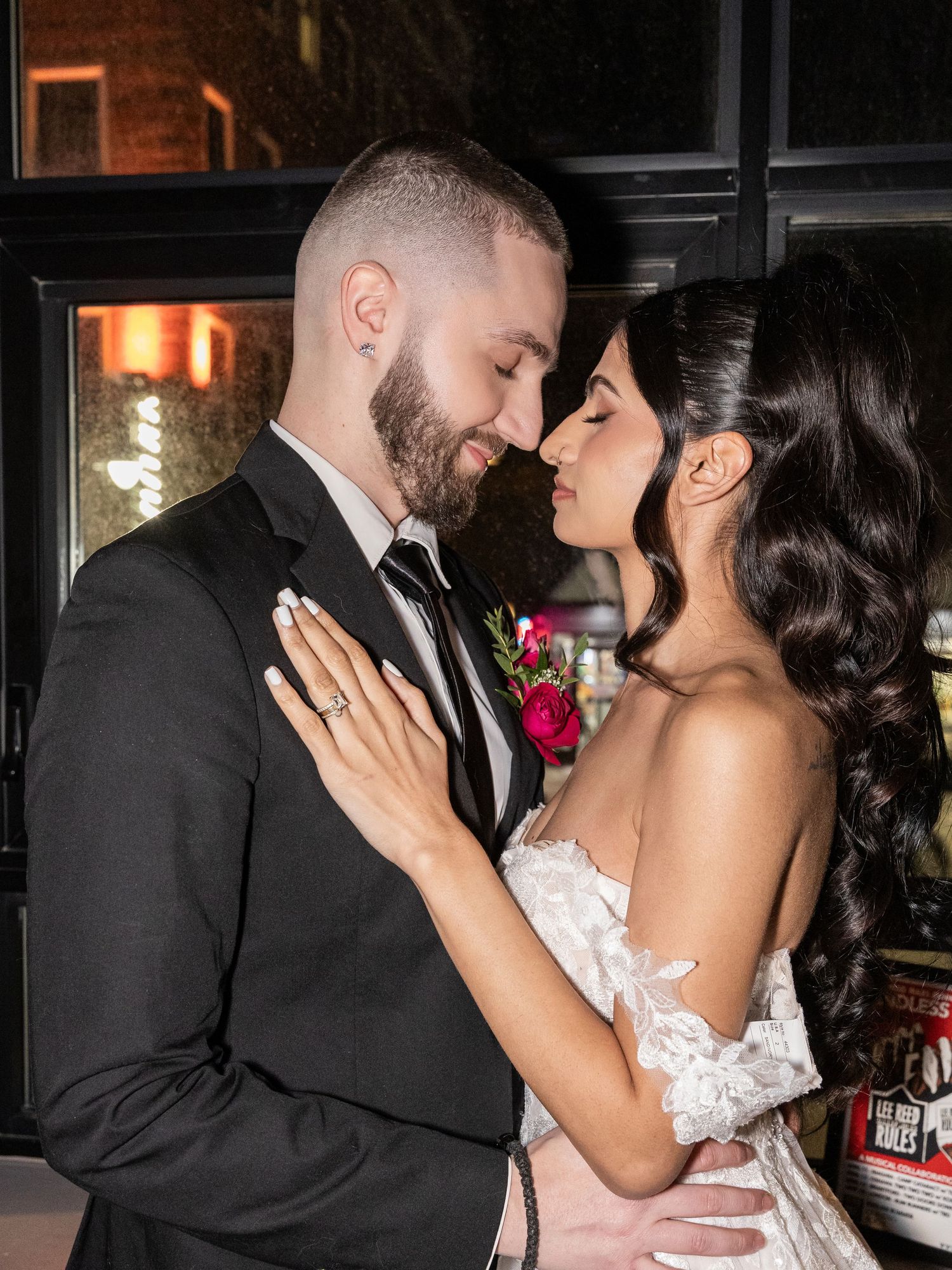 Bride and groom share an intimate forehead touch moment in wedding attire with floral boutonniere.