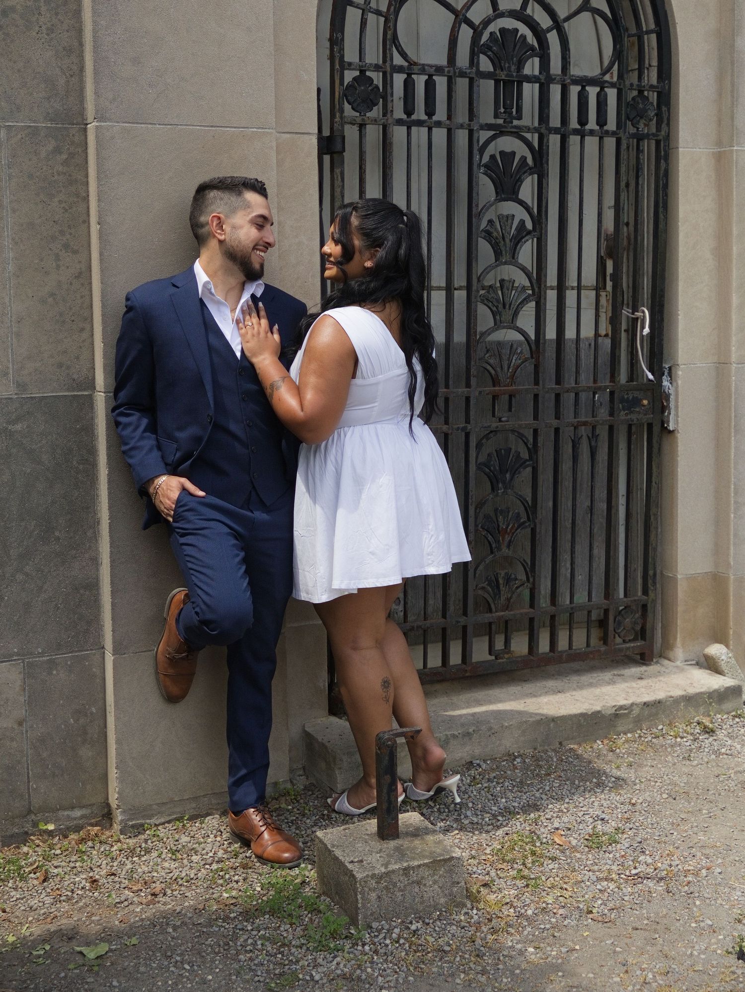 Couple in love leaning against stone wall with ornate iron gate backdrop.