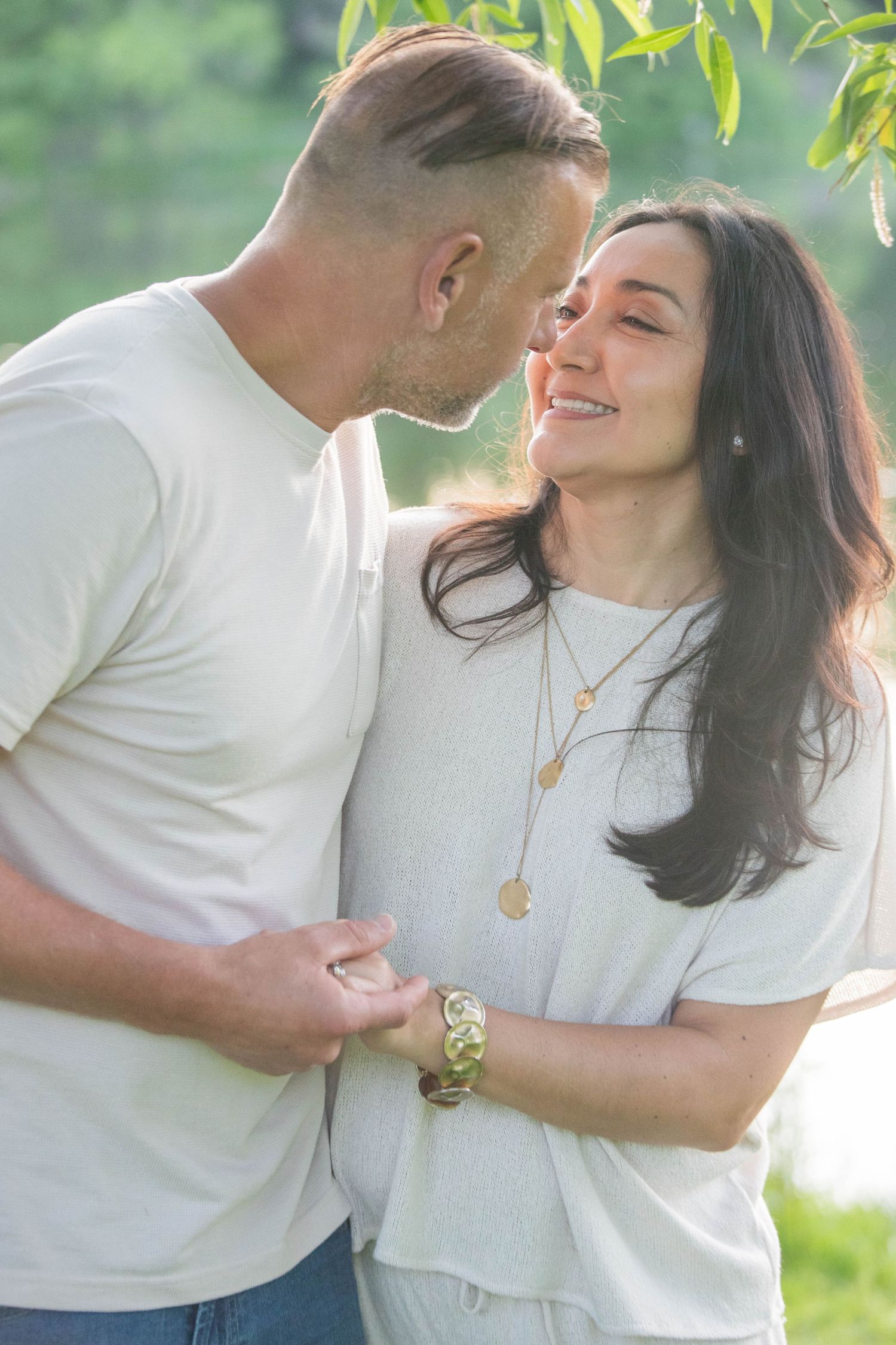 Happy couple sharing tender moment outdoors in sunlit park setting, woman laughing joyfully.