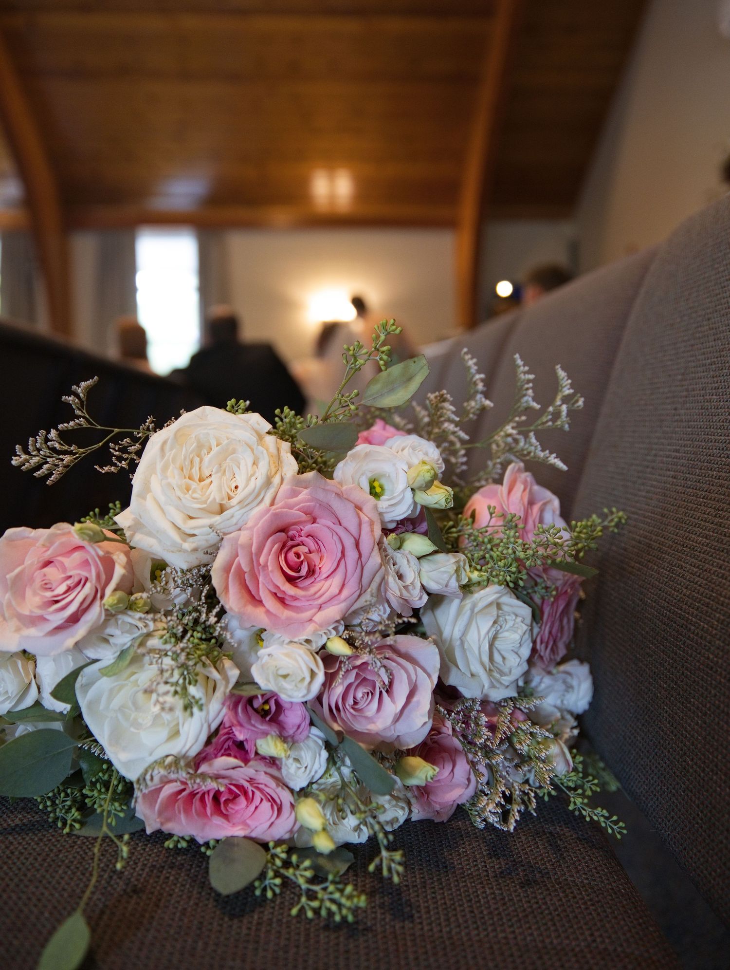 A romantic bridal bouquet of pink and cream roses resting on a church pew during a wedding ceremony.