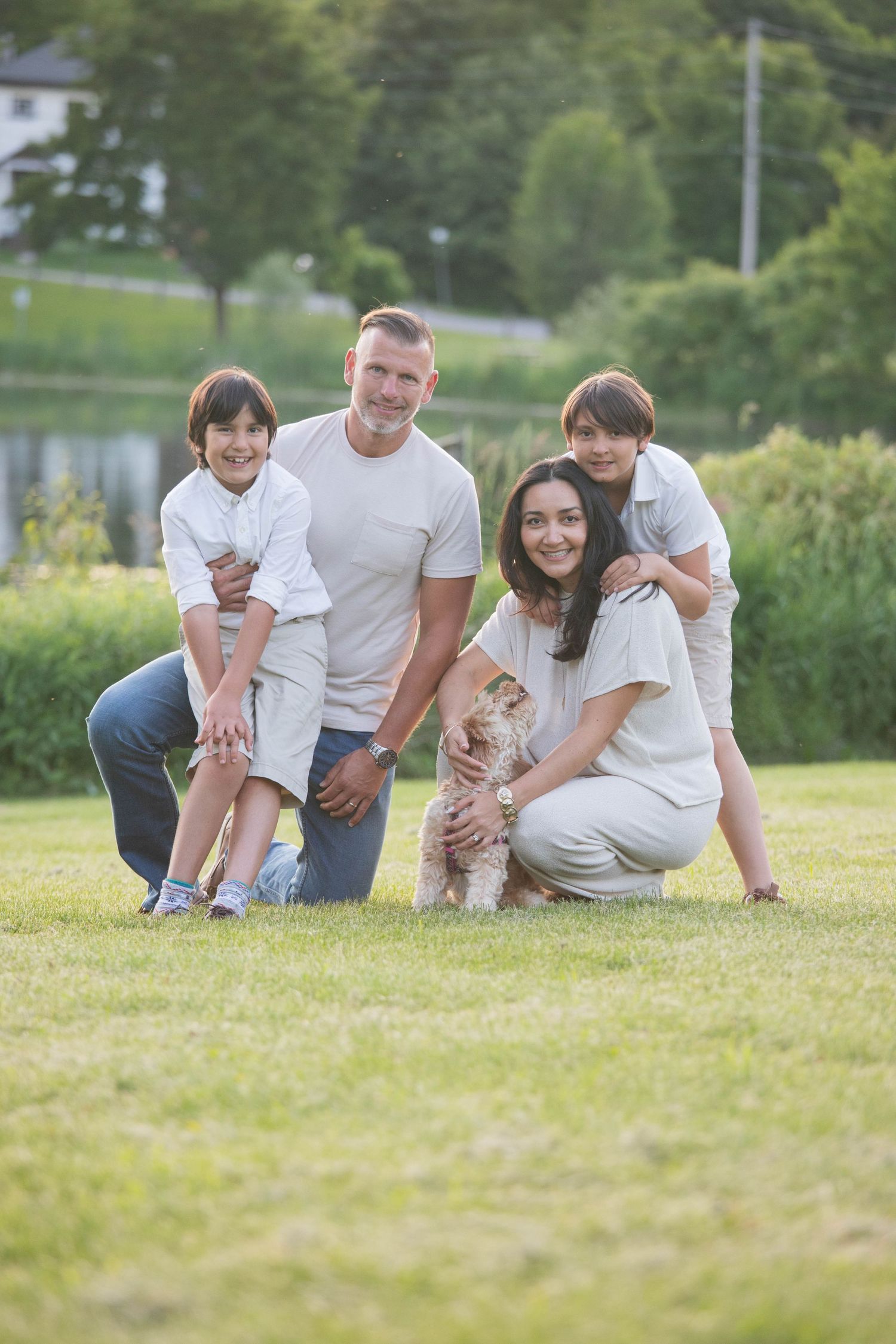 Smiling family of four posing with their fluffy dog on green grass in a park.