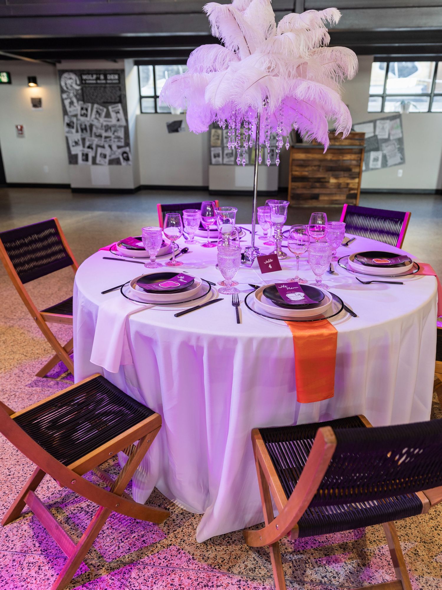 Elegant wedding table with white linens, purple lighting, and tall feather centerpiece.