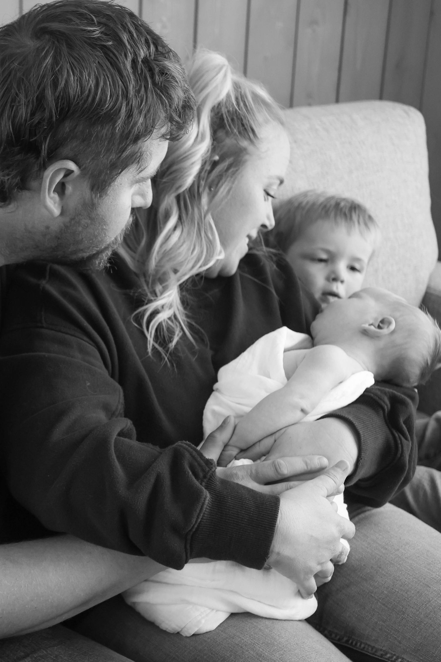 Black and white photo of parents and toddler lovingly gazing at their newborn baby.