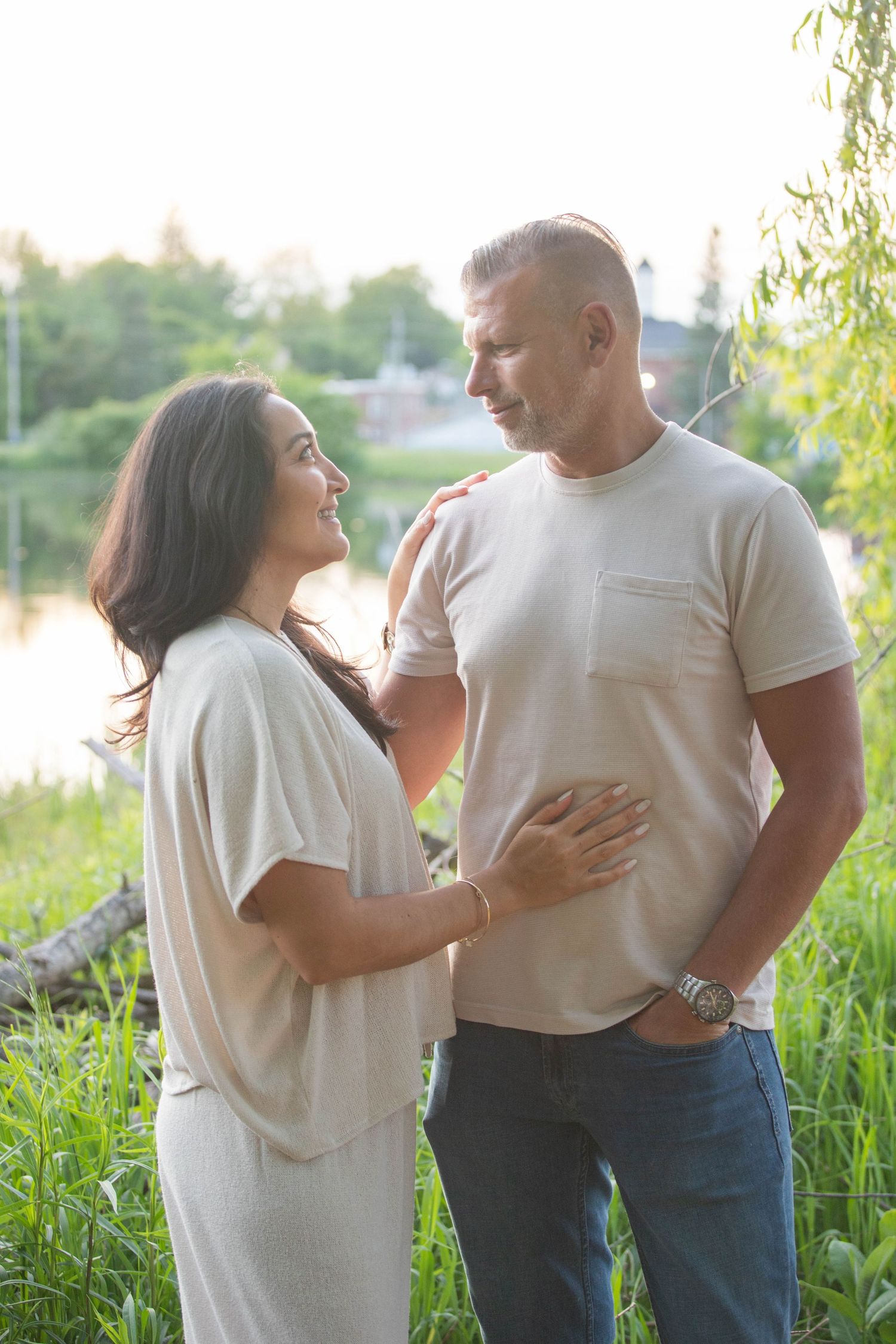 A happy couple stands together near a peaceful lakeside surrounded by green grass.