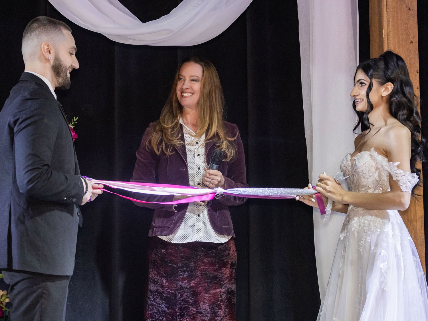 Officiant performs handfasting ceremony with ribbon between bride and groom at wedding altar.