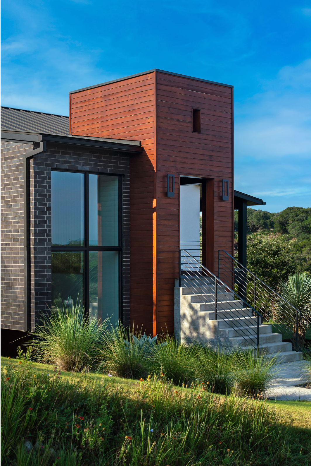 Contemporary home with red cedar tower, brick facade, and steel stair railings.