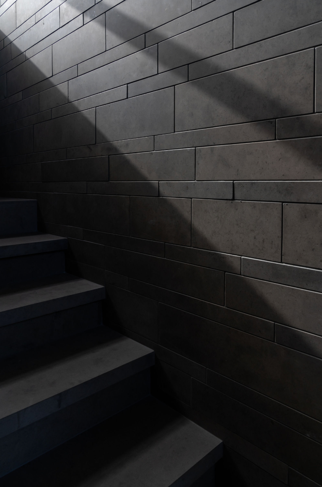 Dark concrete staircase with dramatic light and shadow pattern on textured brick wall in moody interior.