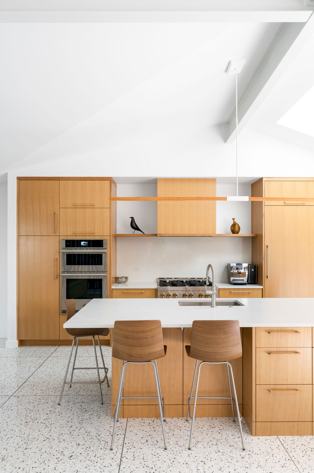 Mid-century modern kitchen featuring warm wood cabinets, white countertop island, terrazzo floors, and vaulted ceiling.