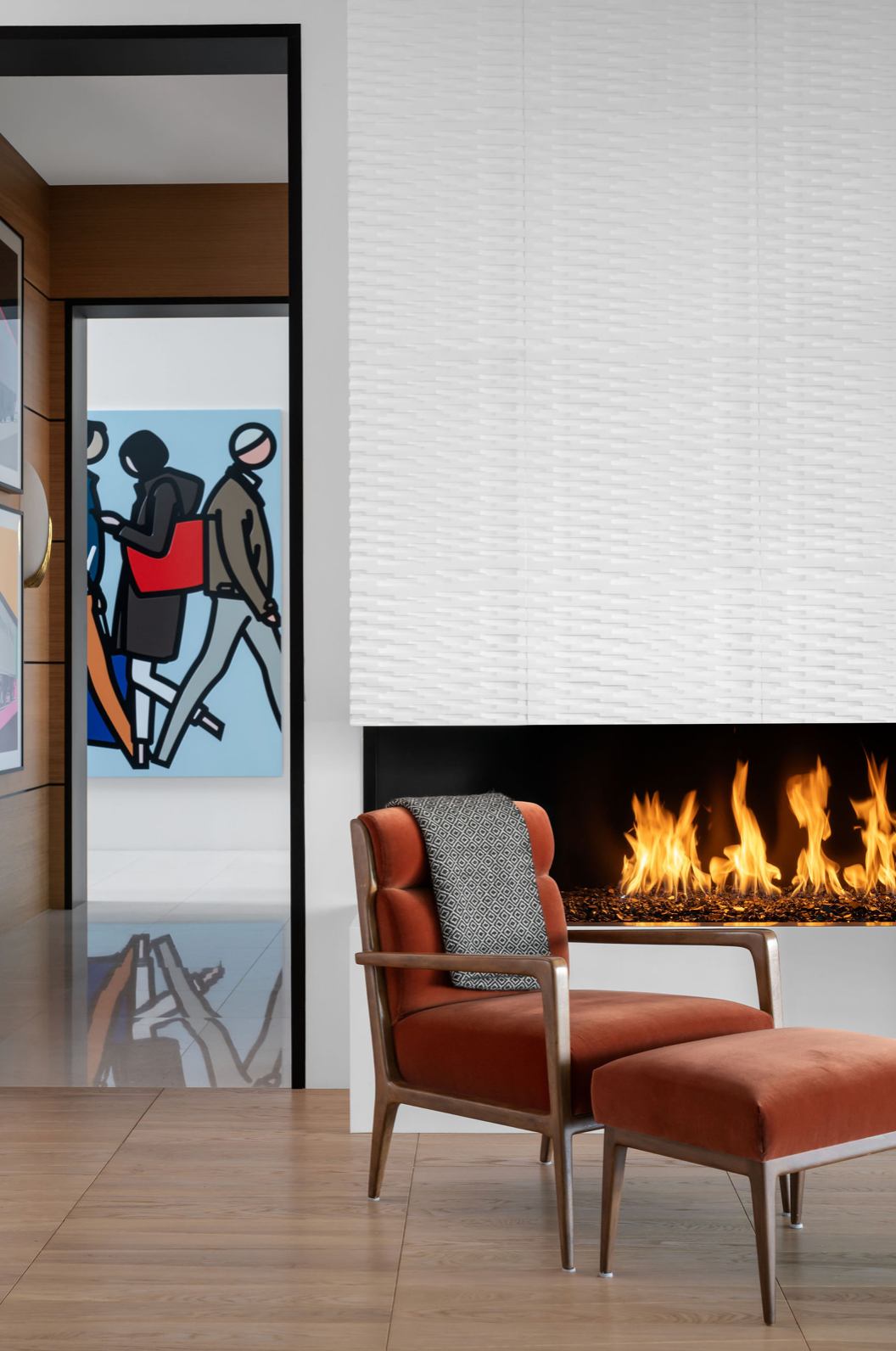 Modern living room with orange lounge chair, linear fireplace, white textured surround, and figurative art.