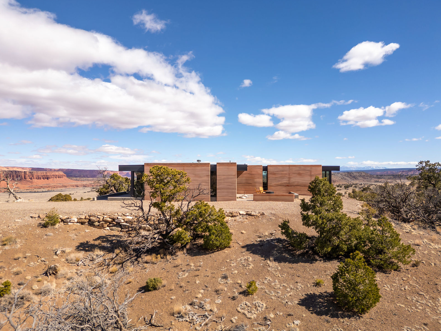 Rustic modern home with wood cladding surrounded by desert scrubland and canyon views.