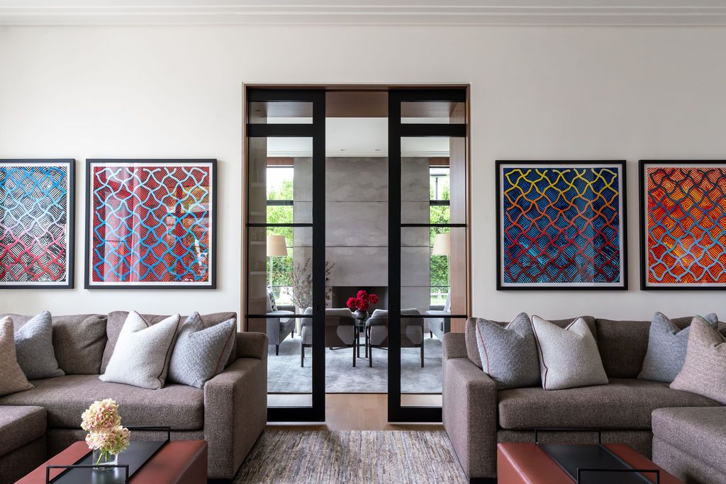 Modern living room with gray sofas, colorful geometric artwork, and glass partition doors.