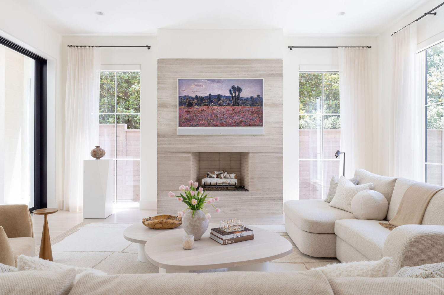 Bright living room with travertine fireplace, cream sofas, round coffee table, and sheer curtains.