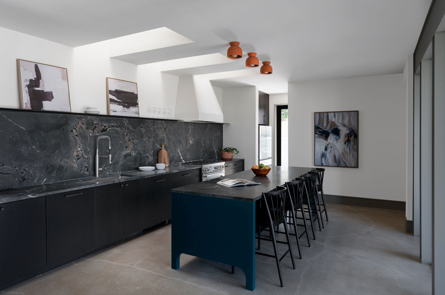 Sleek modern kitchen with dark marble backsplash, navy island, black bar stools, and copper pendant lights.