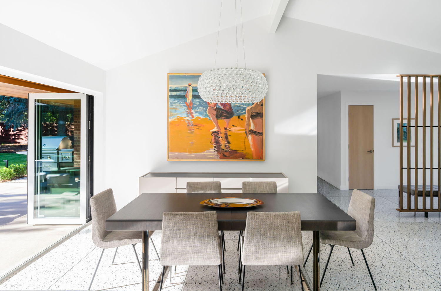 Bright dining room with colorful abstract painting, modern gray chairs, dark table, and terrazzo floors.