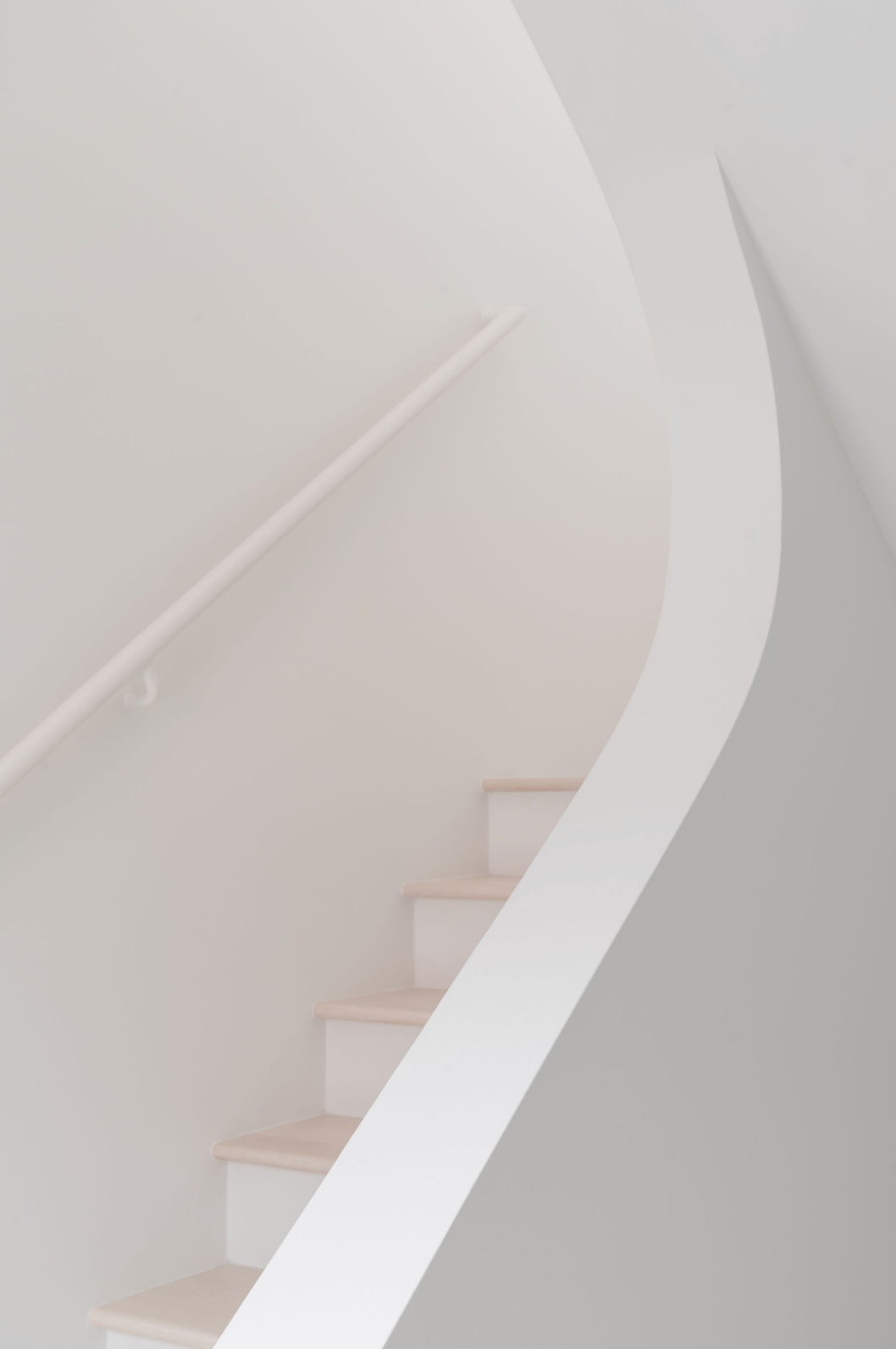 Minimalist white curved staircase with clean lines, white walls, and soft natural light in a modern home.