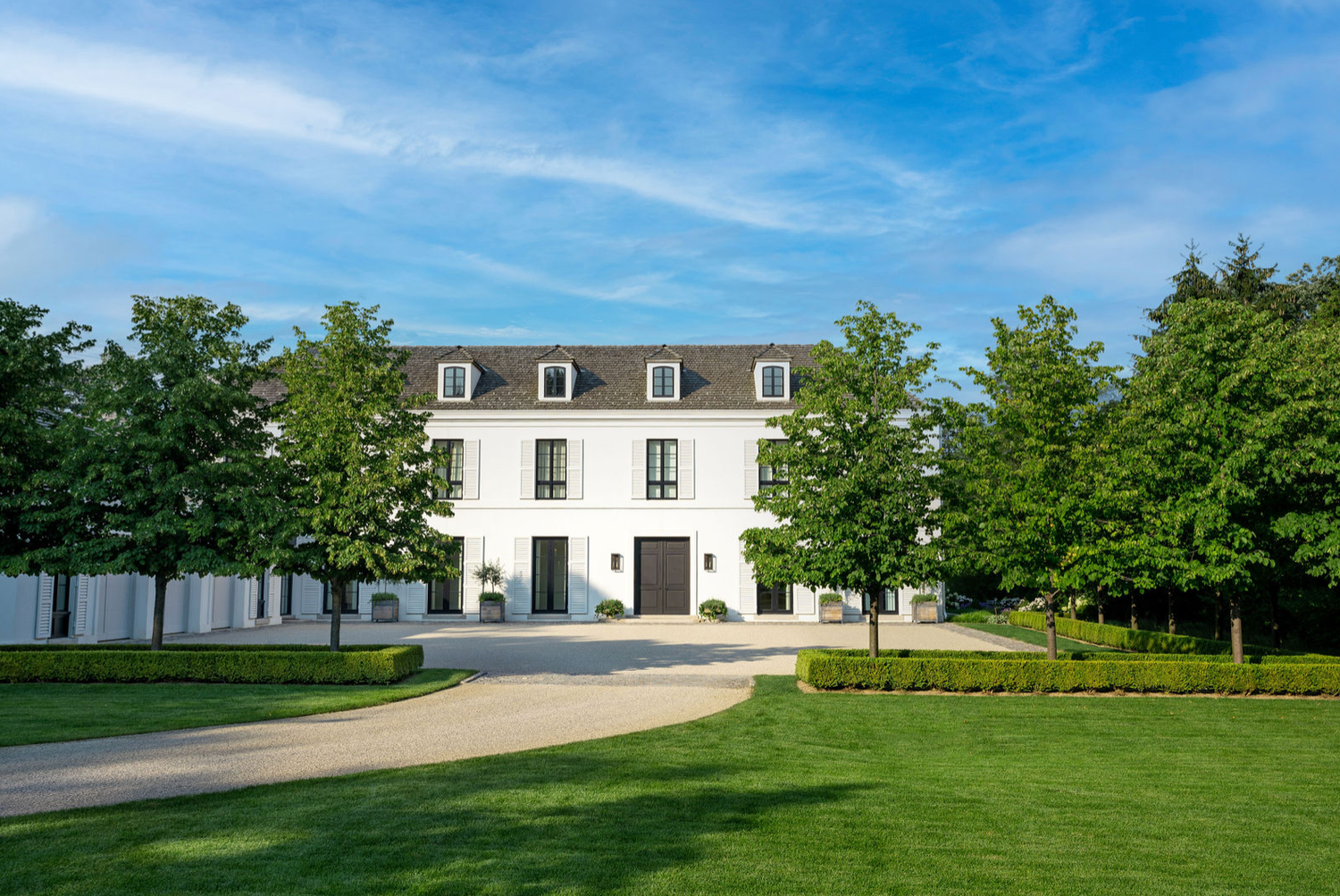 Classic white French-style manor with dormer windows, gravel driveway, and manicured grounds.