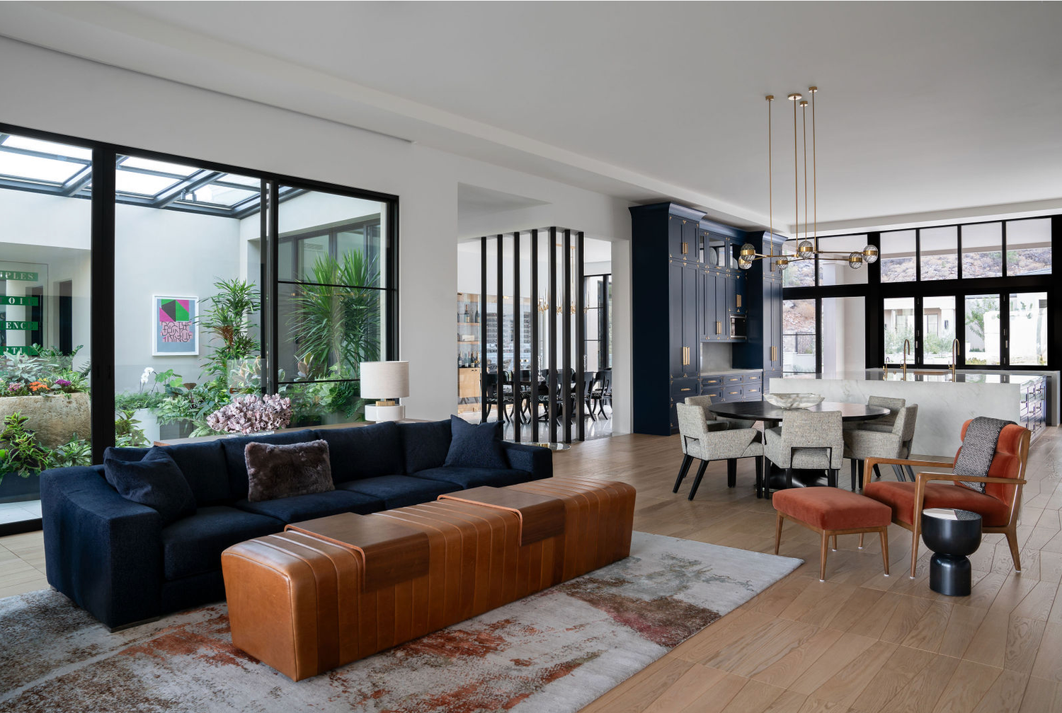 Open-plan living room with navy sofa, leather ottoman, dining area, and floor-to-ceiling garden windows.
