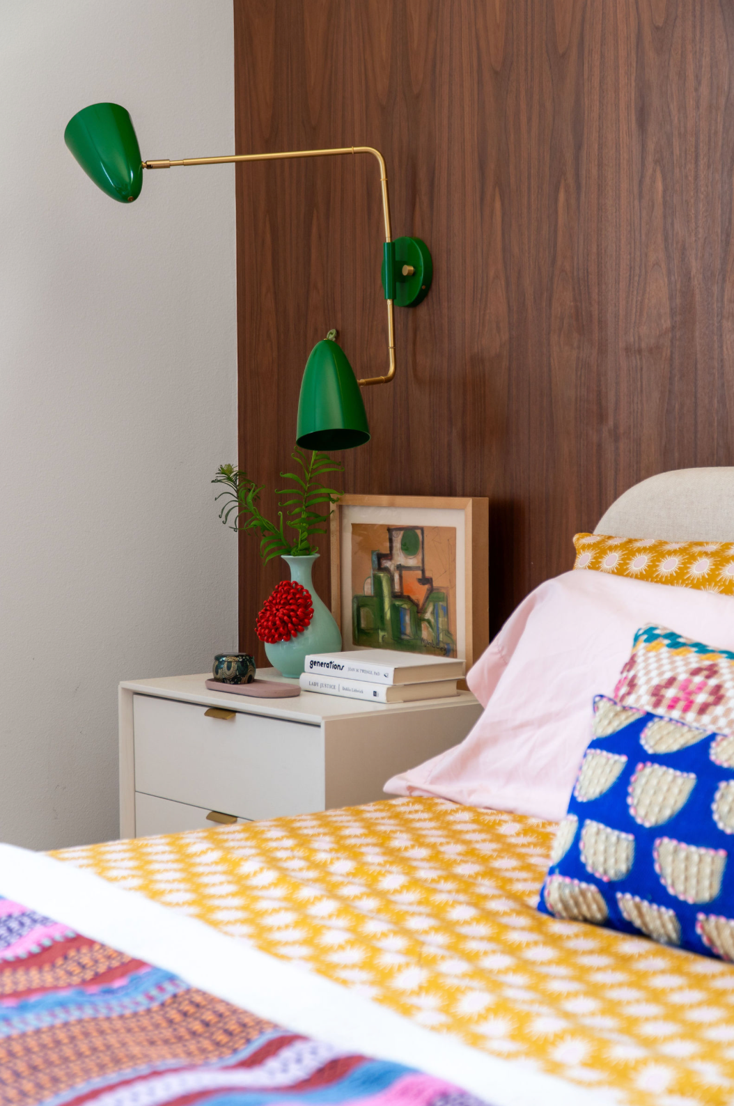 Mid-century bedroom detail with green articulating wall sconce, walnut headboard, and colorful patterned bedding.