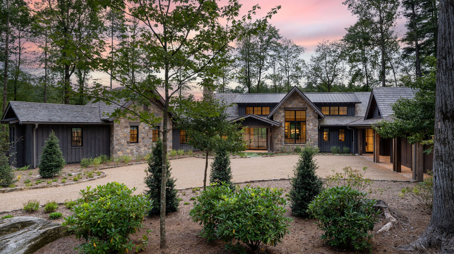 Elegant dark wood and stone luxury home surrounded by tall pines at sunset.
