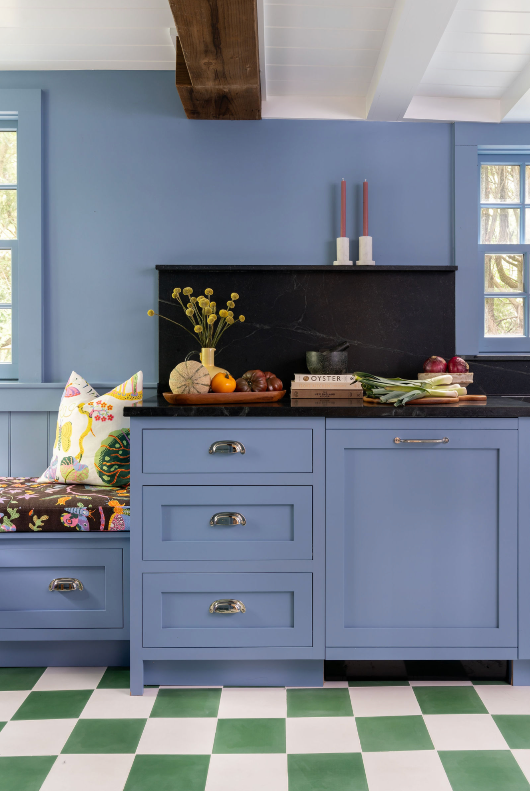 Blue kitchen with shaker cabinets, black marble backsplash, green checkered floor, and built-in bench seating.