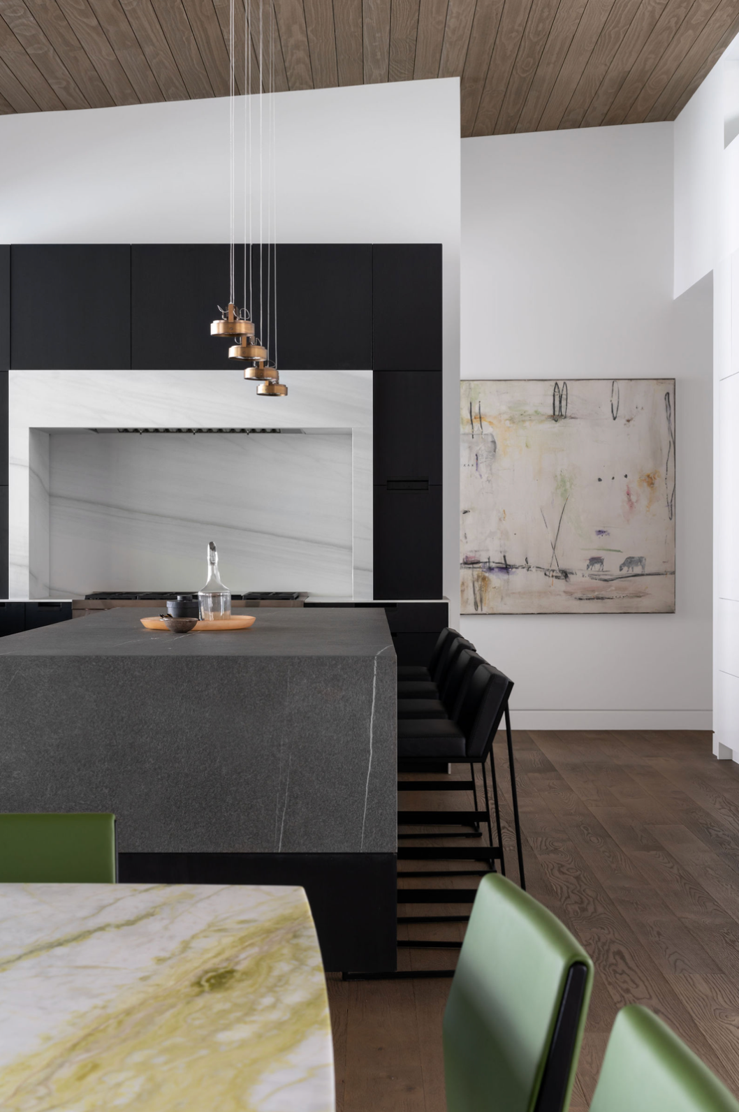 Contemporary kitchen with dark granite island, black cabinetry, marble dining table, and abstract artwork on white wall.