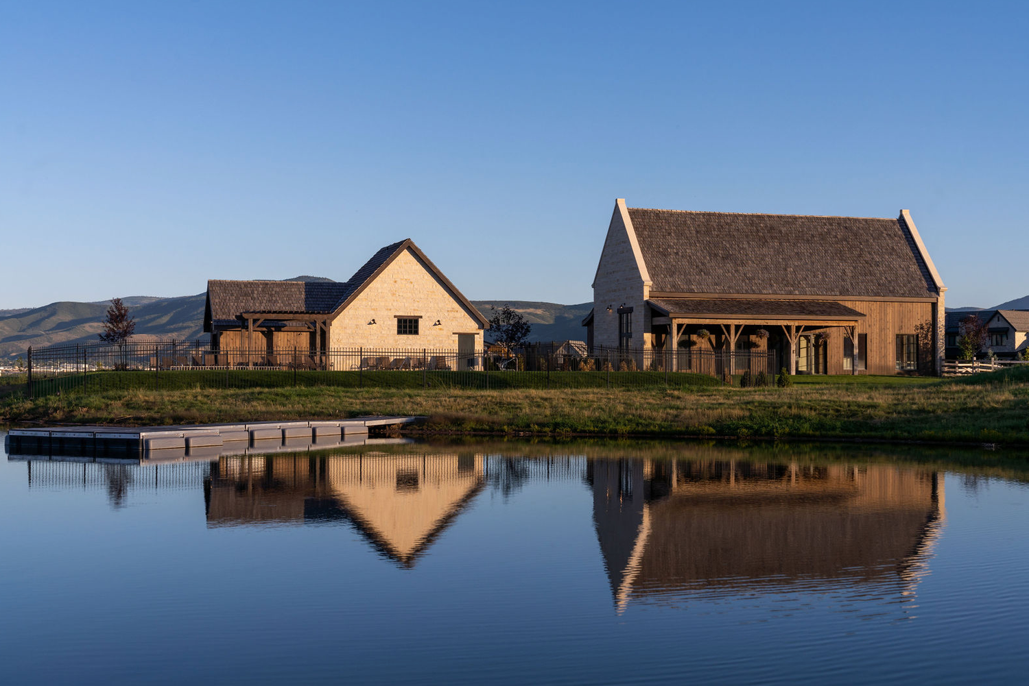 Rustic farmstead buildings with wood and stone construction perfectly reflected in a calm pond at golden hour.