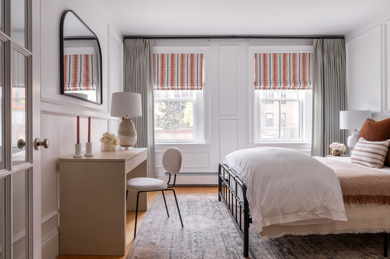 Cozy bedroom with black iron bed, striped orange roman shades, gray curtains, and a vintage-style area rug.