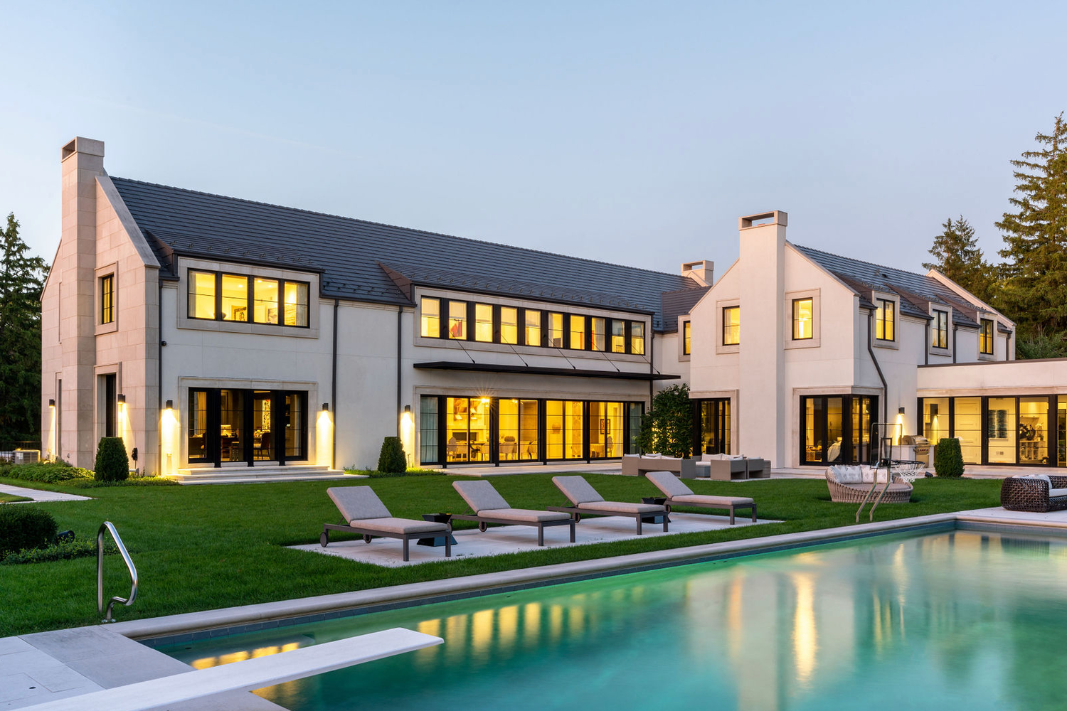 Elegant white luxury home with manicured lawn and sparkling pool photographed at twilight.