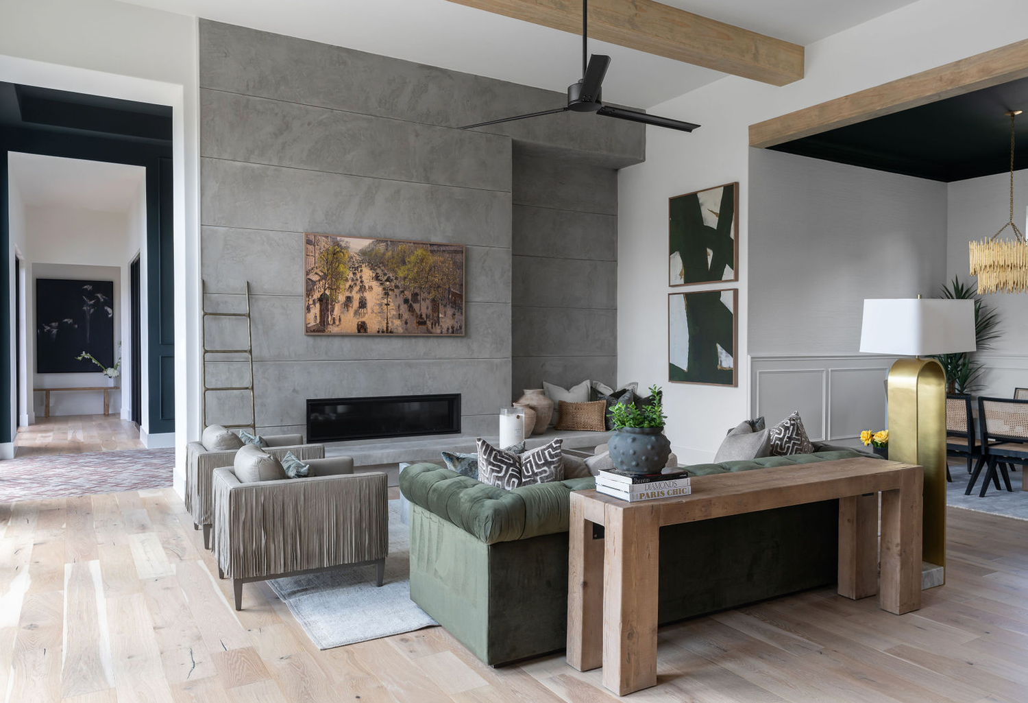 Contemporary living room with gray concrete fireplace wall, green velvet sofa, wood beam ceiling, and light hardwood floors.