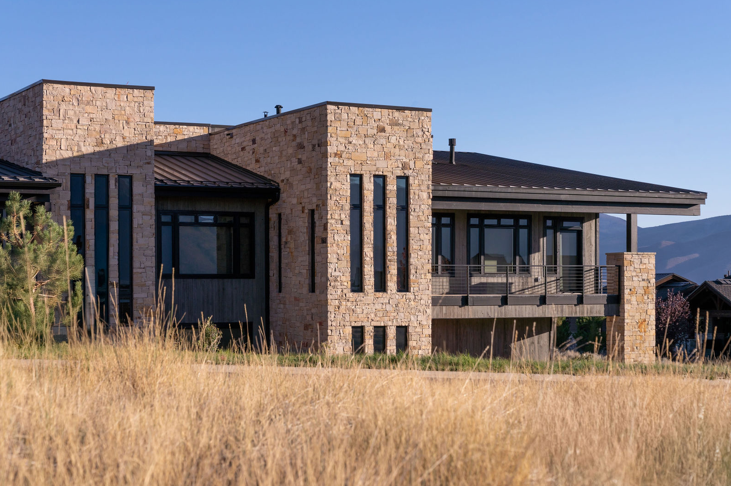 Contemporary brick and stone ranch home with metal roof surrounded by golden native grasses and mountain views.