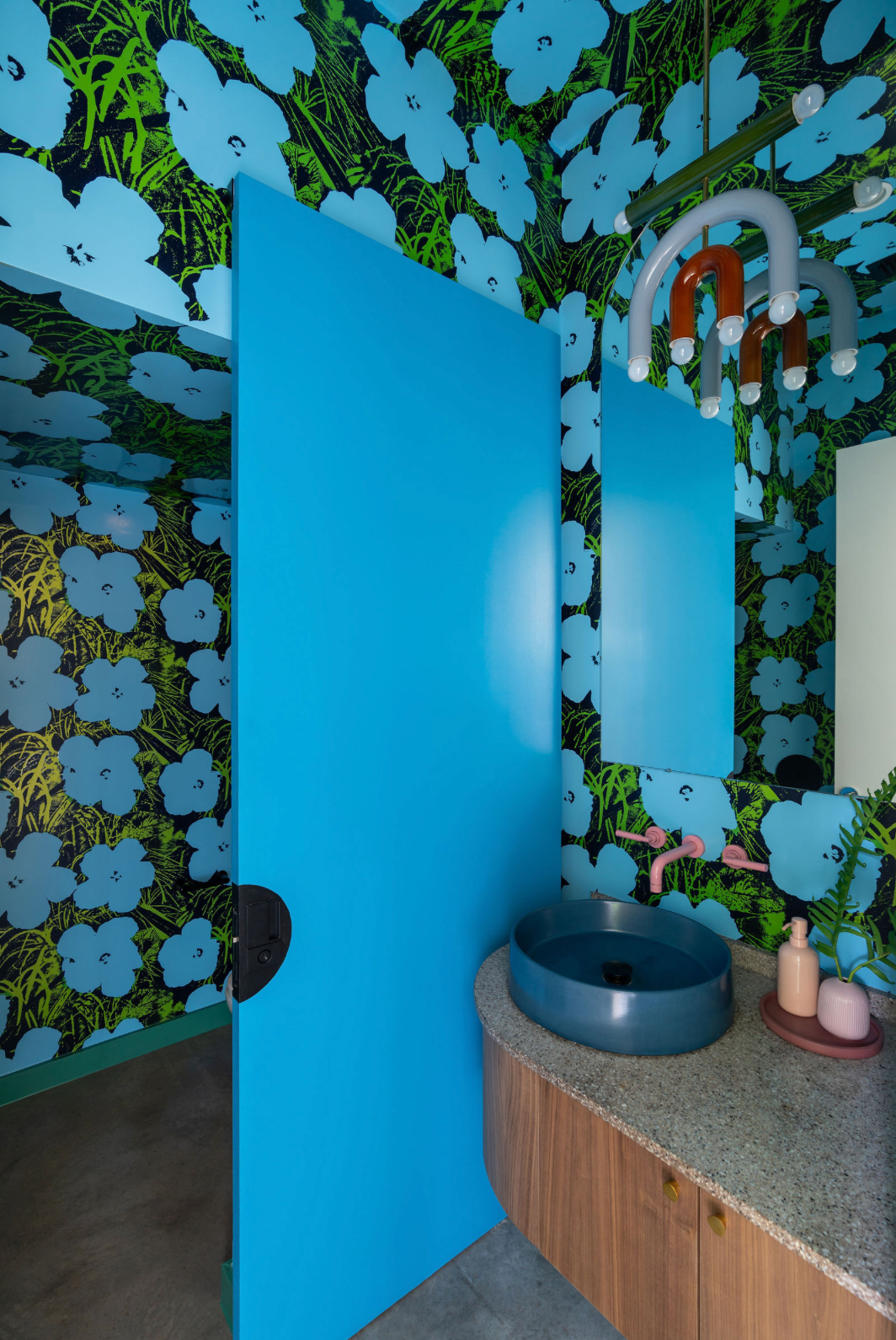 Bold bathroom with blue floral Andy Warhol wallpaper, blue vessel sink, and vibrant cyan accent wall.