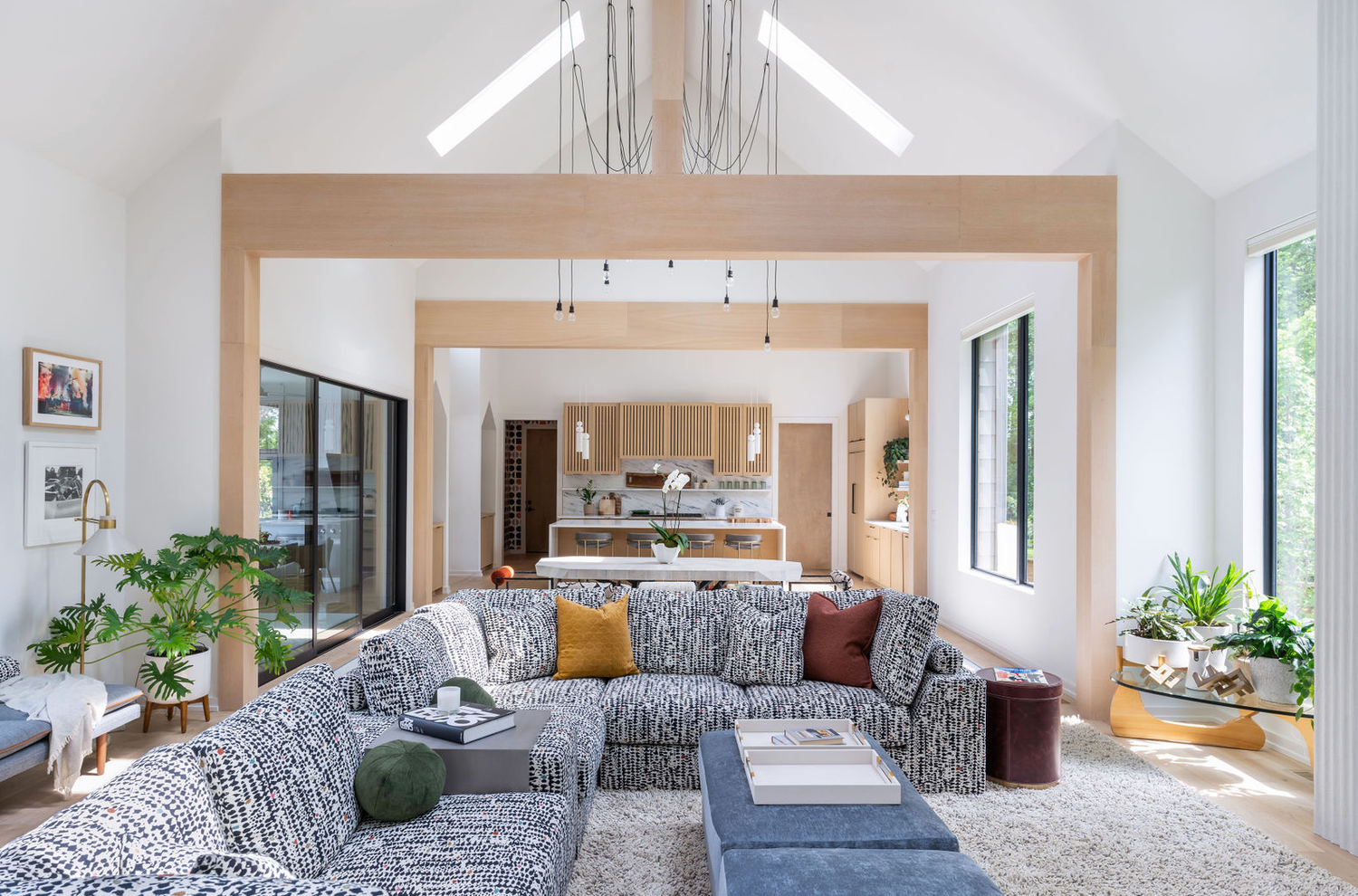 Spacious modern living room with large gray sectional sofa, vaulted ceiling, and open kitchen in background.