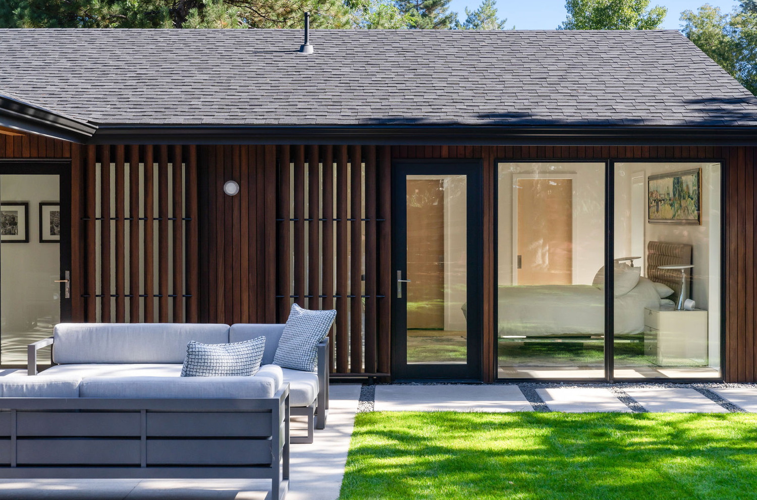 Mid-century modern home exterior with wood slat accents, large sliding glass doors, and manicured green lawn.