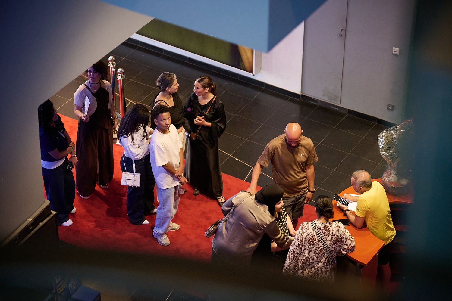 Group of people gathered on a red carpet inside a modern building, viewed from above.