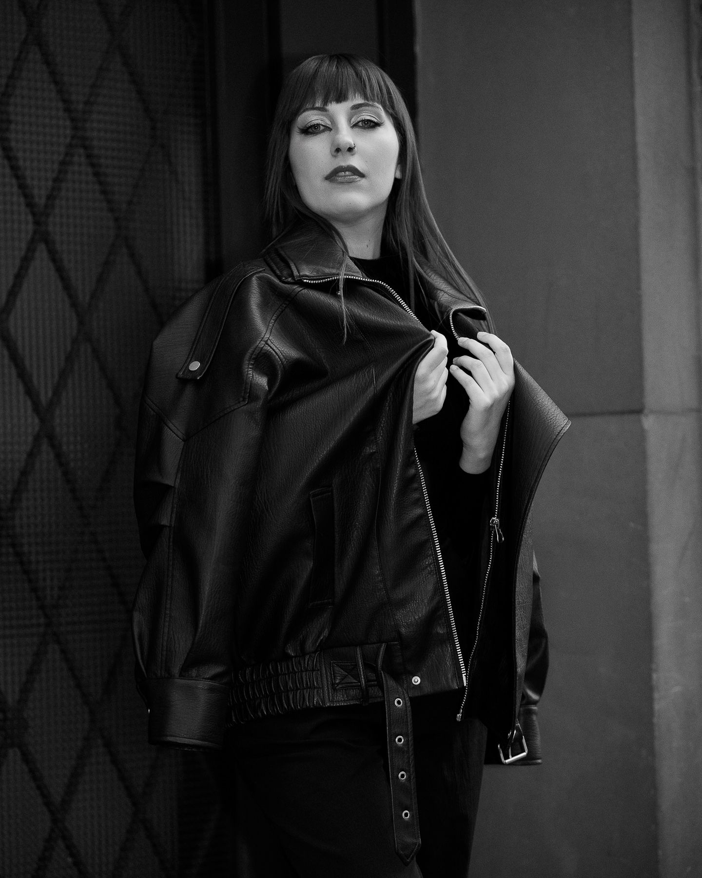 Woman in black leather jacket posing dramatically in a black and white urban fashion portrait.