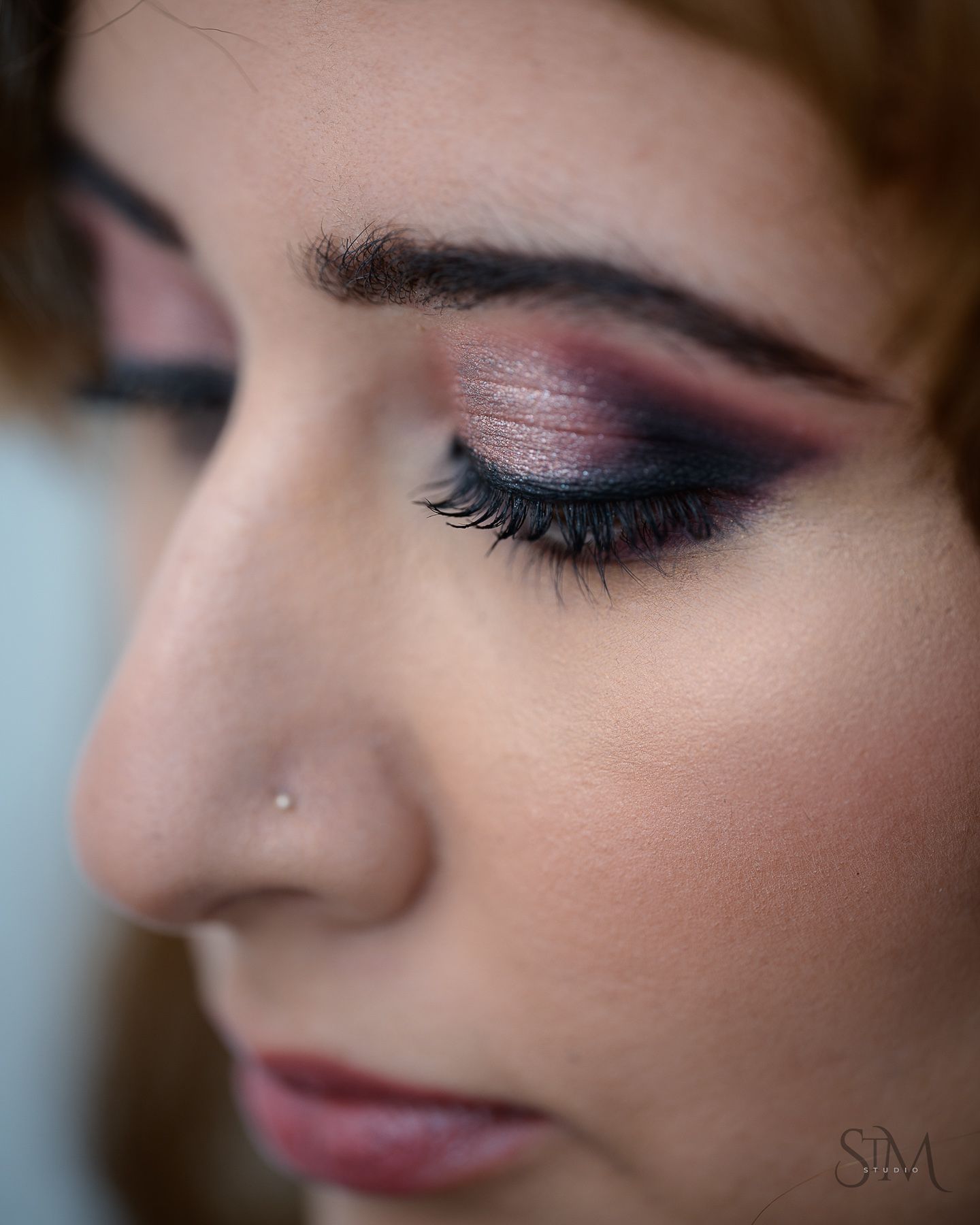 Close-up profile of a woman wearing dramatic smoky eye makeup with pink and black eyeshadow and a nose stud.