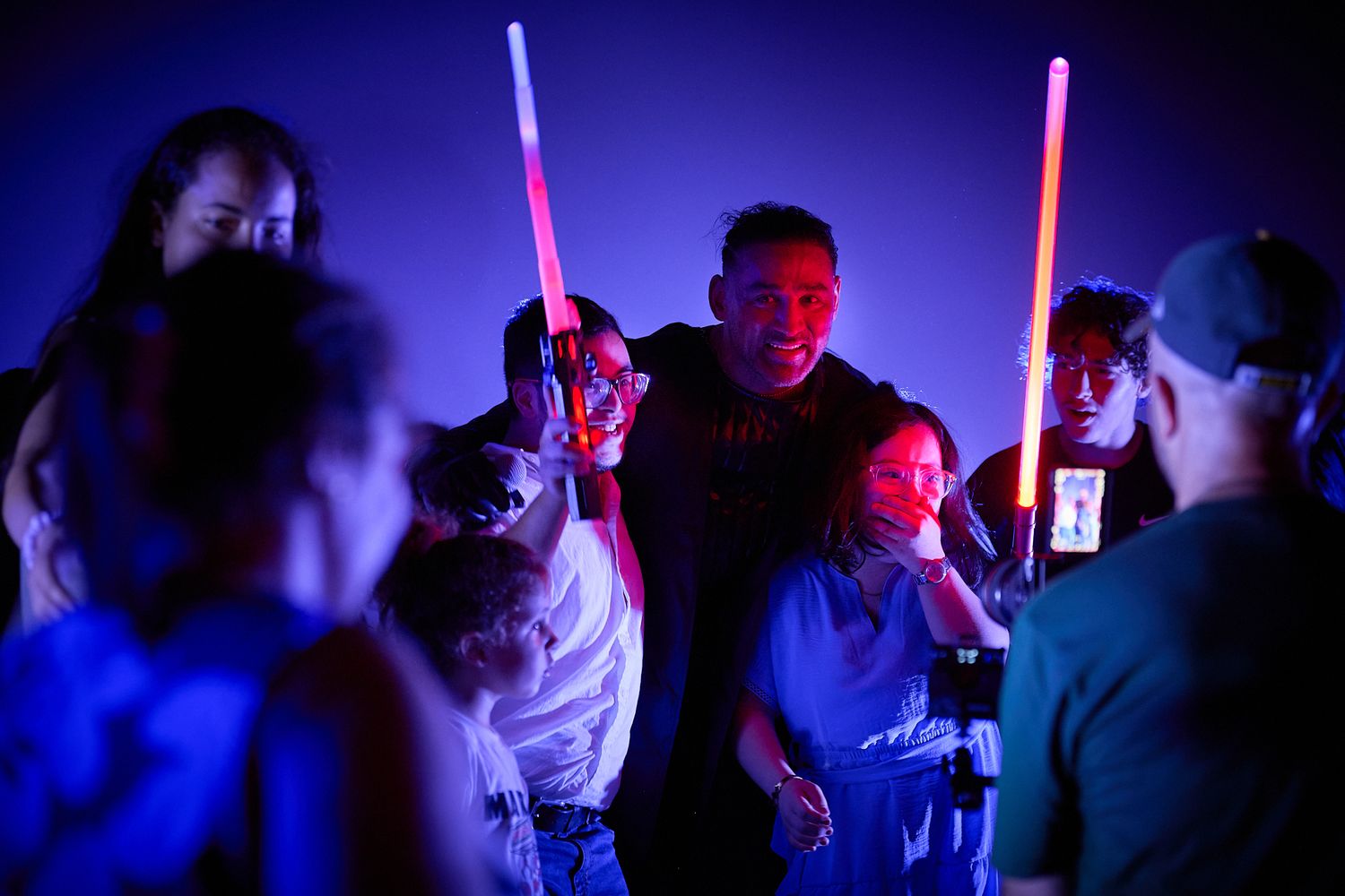 Group of people posing with glowing red and blue lightsabers at a Star Wars themed party event.