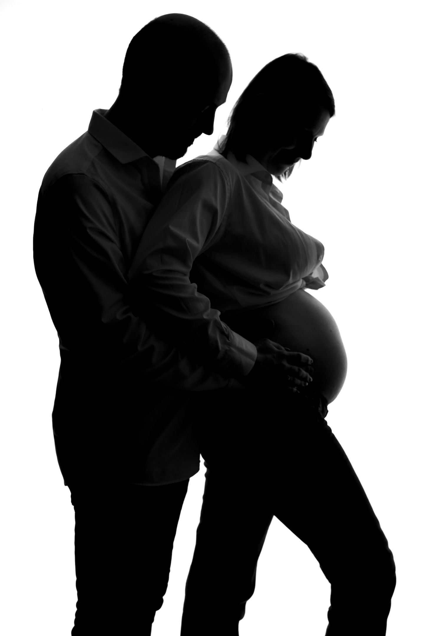 Silhouette of a couple expecting a baby, with the man embracing the pregnant woman from behind on white background.