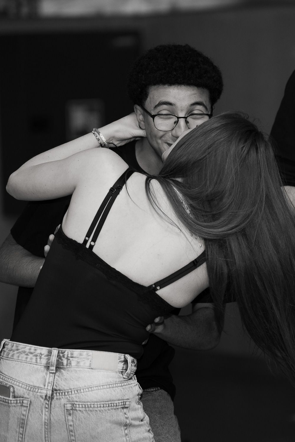 Black and white photo of a young couple sharing a warm embrace at a social gathering.